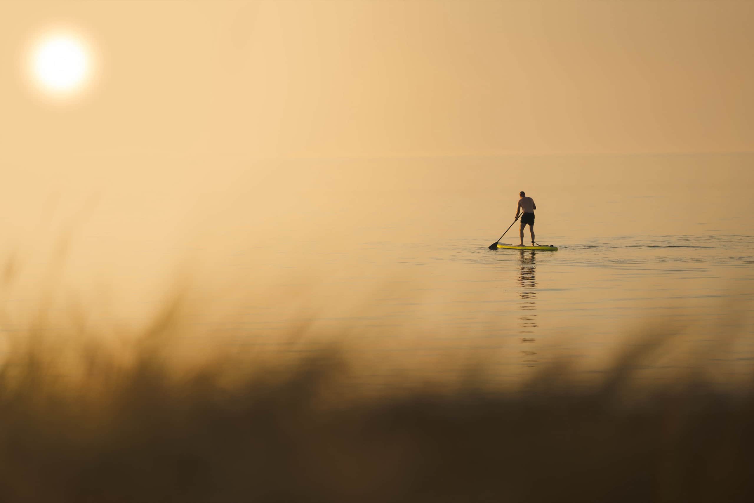 A paddleboarder crossing calm water at sunrise
